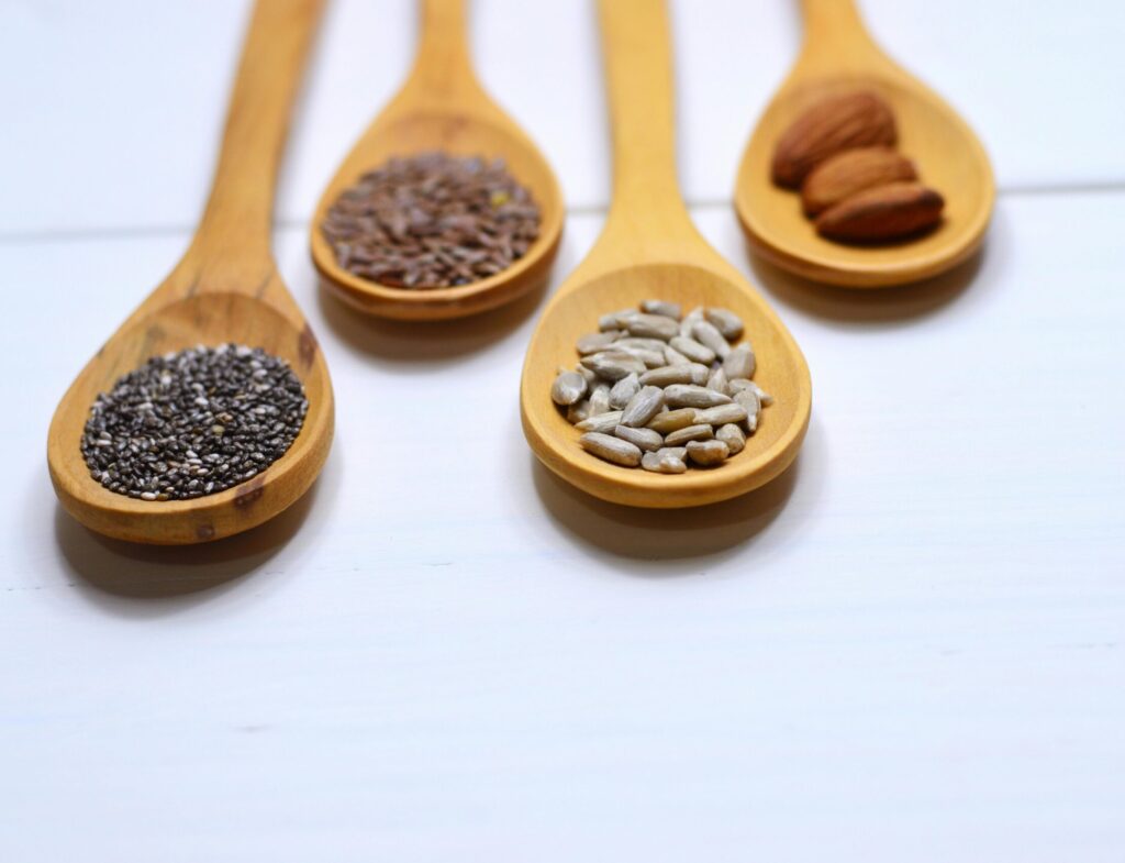Close-up of various nuts and seeds in wooden spoons on a white background, showcasing healthy food options.